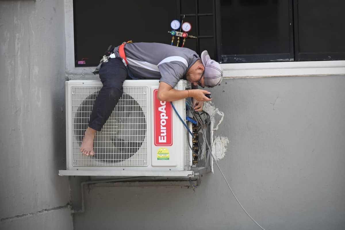 HVAC technician repairing a unit mounted on a building wall