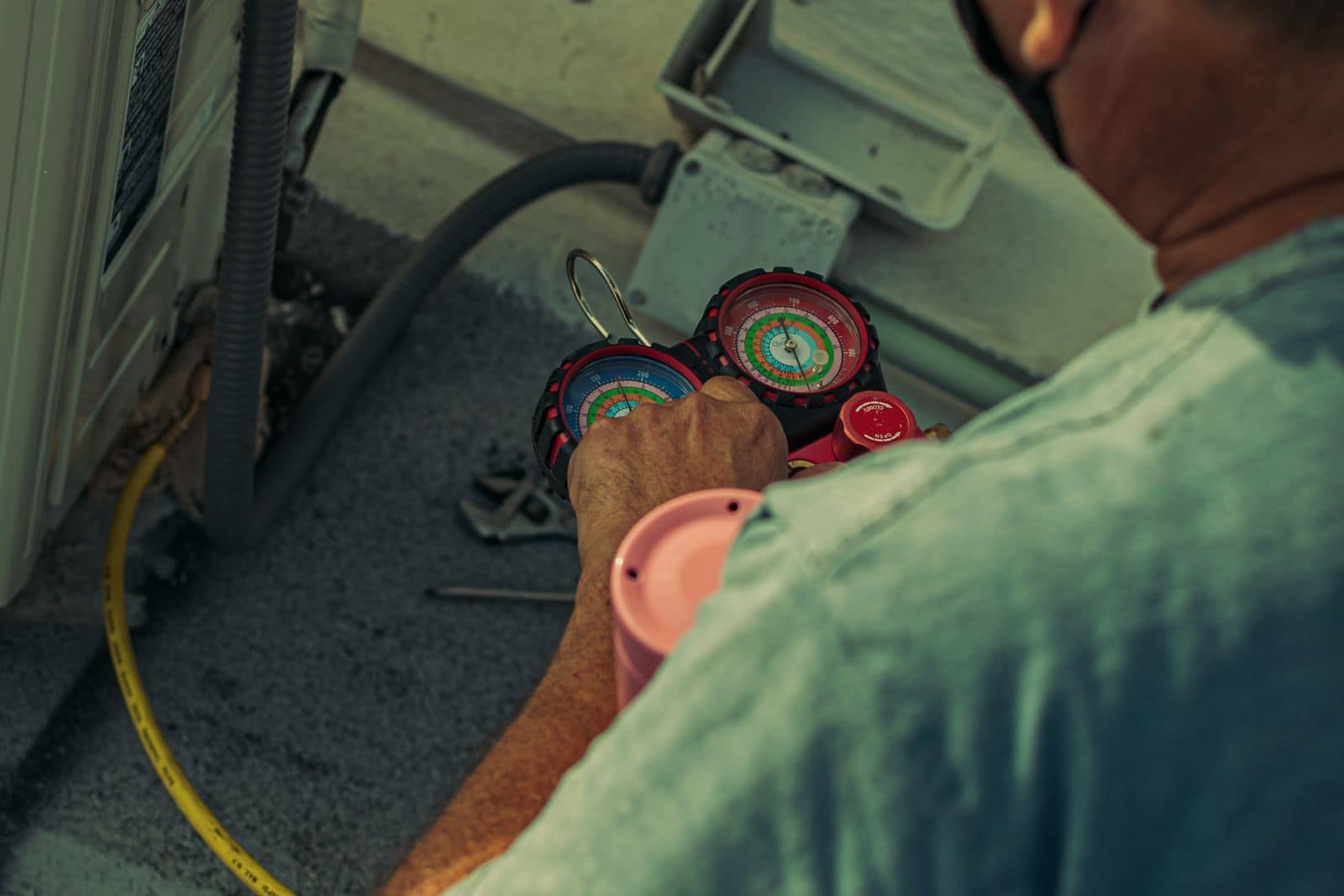 HVAC technician servicing an outdoor condenser unit with gauges